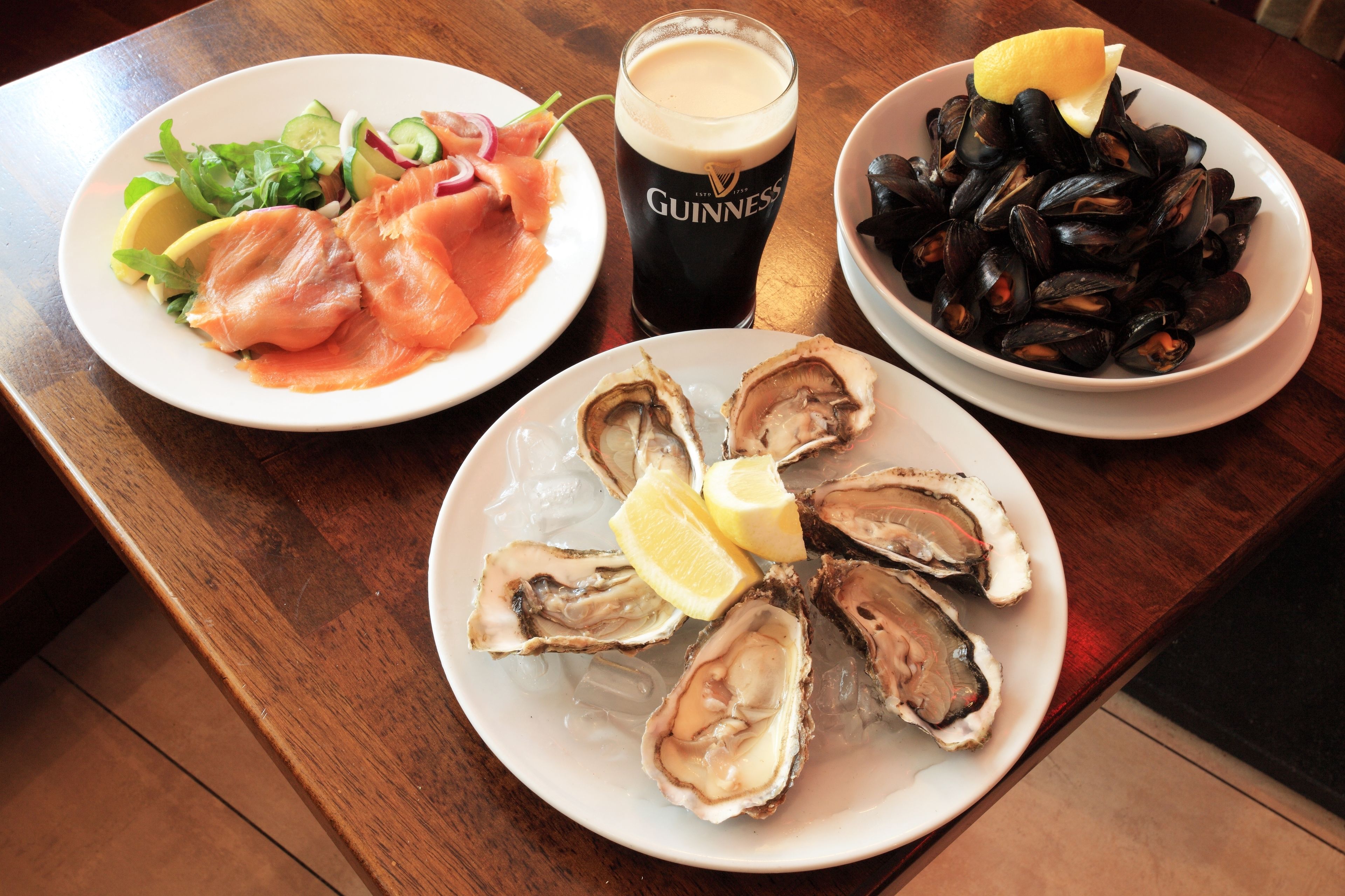 Una mesa con platos de ostras, mejillones y salmón ahumado, una jarra de cerveza Guinness y una ensalada.