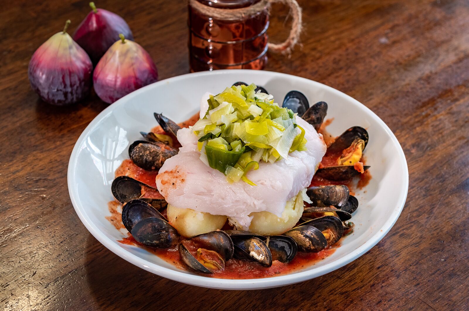 Plato de mariscos con mejillones y pescado, acompañado de cebollas rojas y una copa de bebida roja.