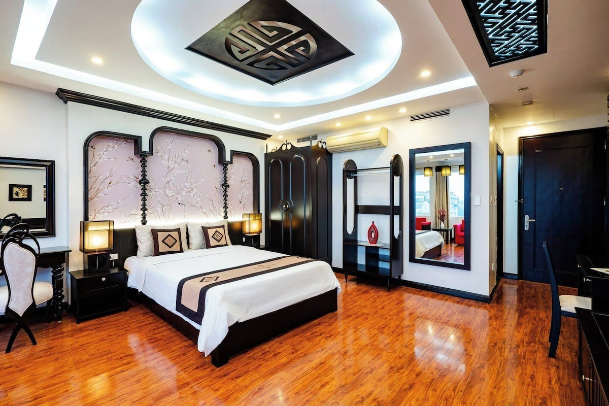 A modern hotel room with a large bed, a vanity with a mirror, and a seating area with a red chair.