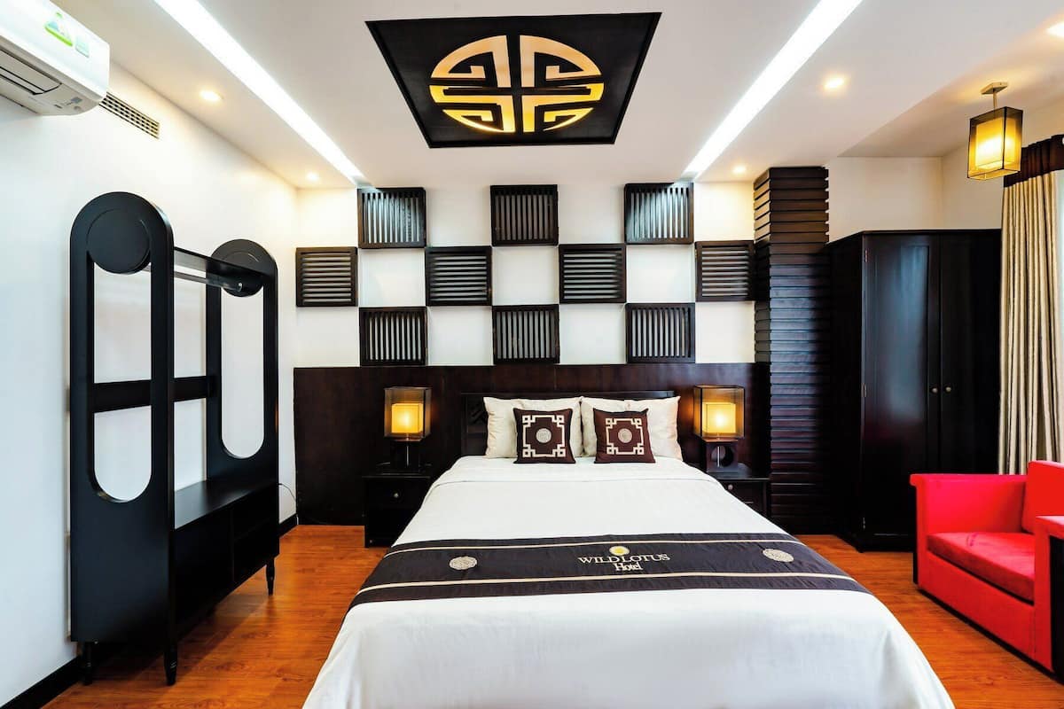 A hotel room with a bed, a red chair, and a unique wall design.