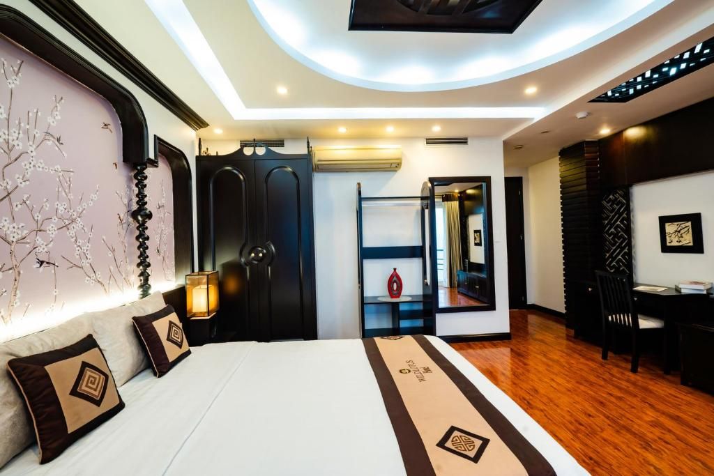 A modern hotel room with a large bed, a bedside table, a desk, and a chair.