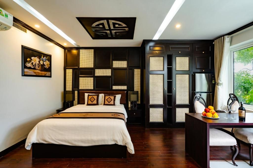A hotel room with a bed, a desk with a chair, a window, and a decorative ceiling piece.