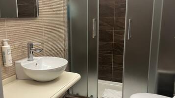 Un bagno moderno con un lavandino capiente, il water e una doccia a pavimento.
