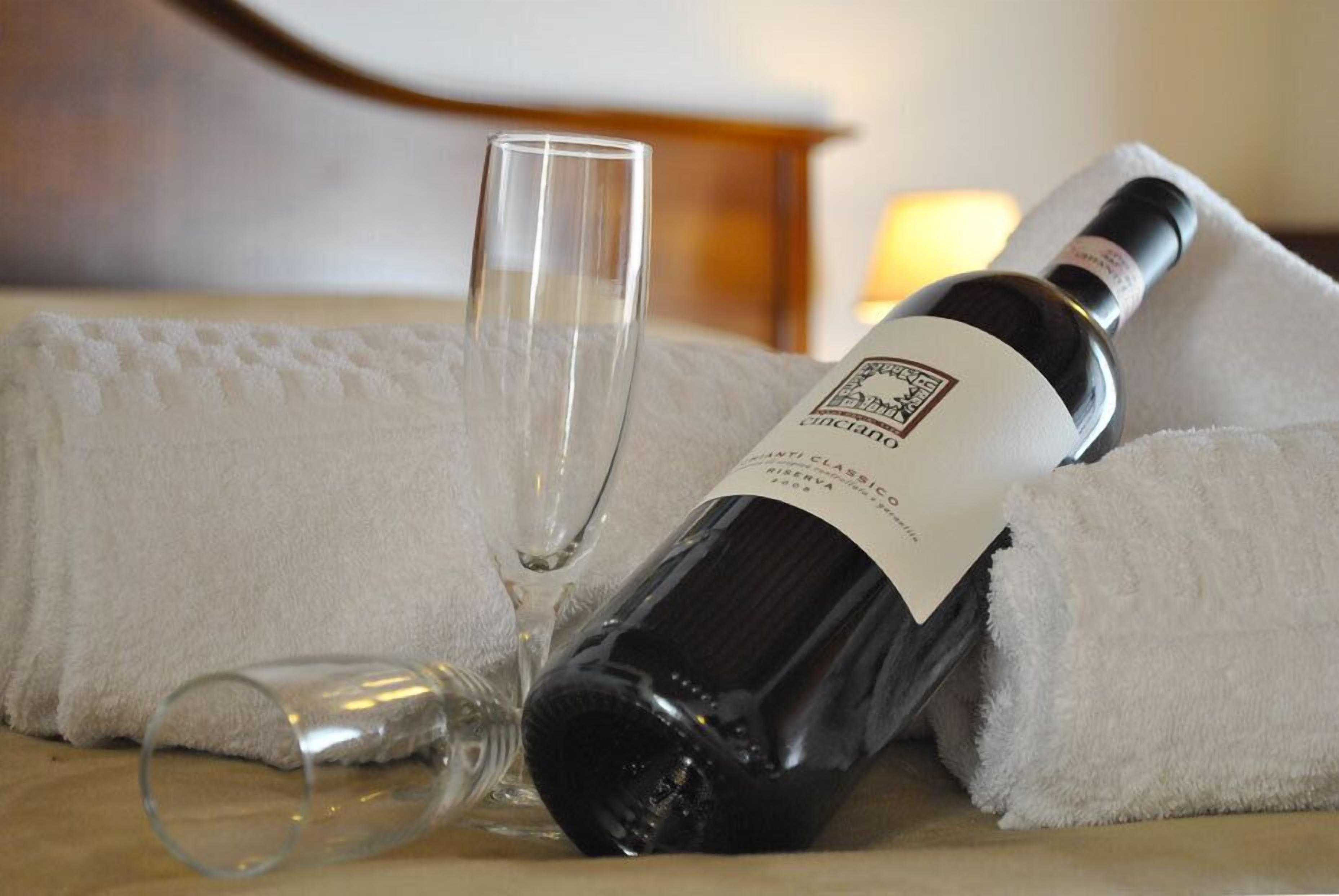 A bottle of wine and a glass on a bed with a white towel.
