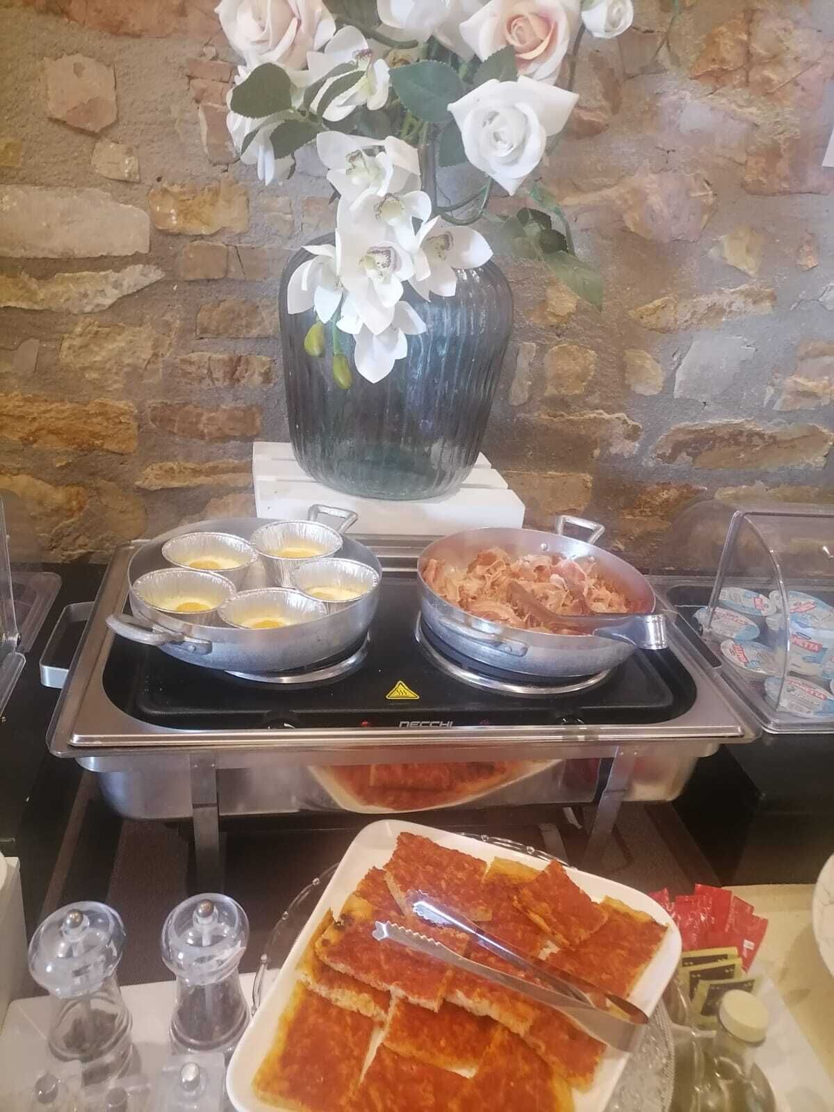 A buffet setup with various food items, including pasta and a dish with meat, in a room with a stone wall background.