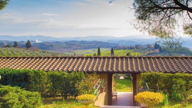 Un espace extérieur abrité, doté d’un toit en tuiles, entouré d’une végétation luxuriante et offrant une vue sur des collines lointaines.