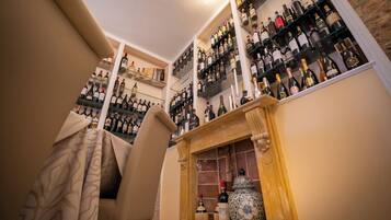 A wine cellar with shelves of bottles, a wooden chair, and a large decorative vase.