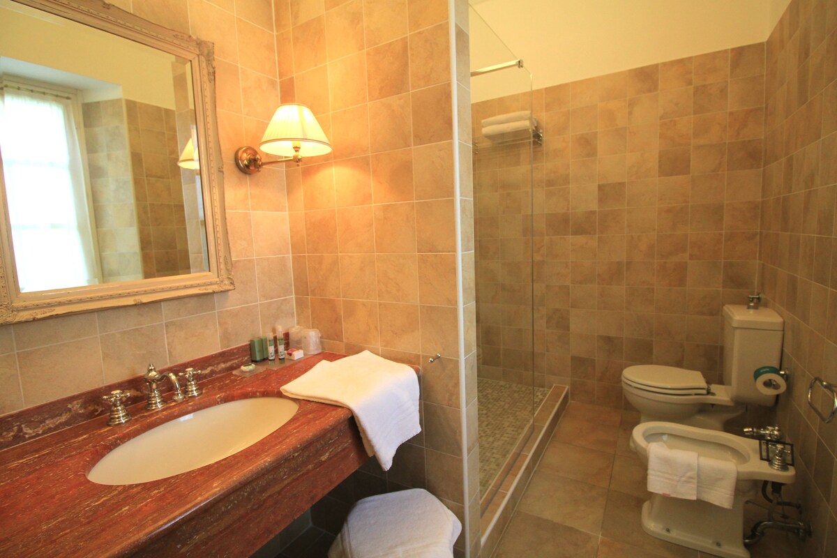 Un baño con lavamanos de mármol, cabina de ducha con paredes de vidrio y un inodoro.