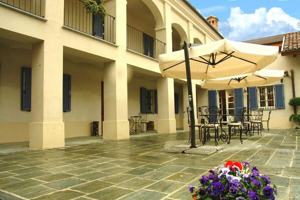 A courtyard with stone flooring, outdoor furniture, and a flower arrangement. - Agriturismo Marcarini (Neviglie)