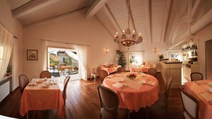 A dining area with round tables, chairs, and a chandelier. There is a view of an outdoor patio through a doorway. - Agriturismo Marcarini (Neviglie)