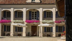 A building with a tiled roof, arched windows, and outdoor seating with umbrellas. - Agriturismo Marcarini (Neviglie)