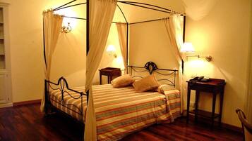 A four-poster bed with a striped bedspread and two pillows, flanked by nightstands with lamps, in a room with wooden flooring and plain walls.