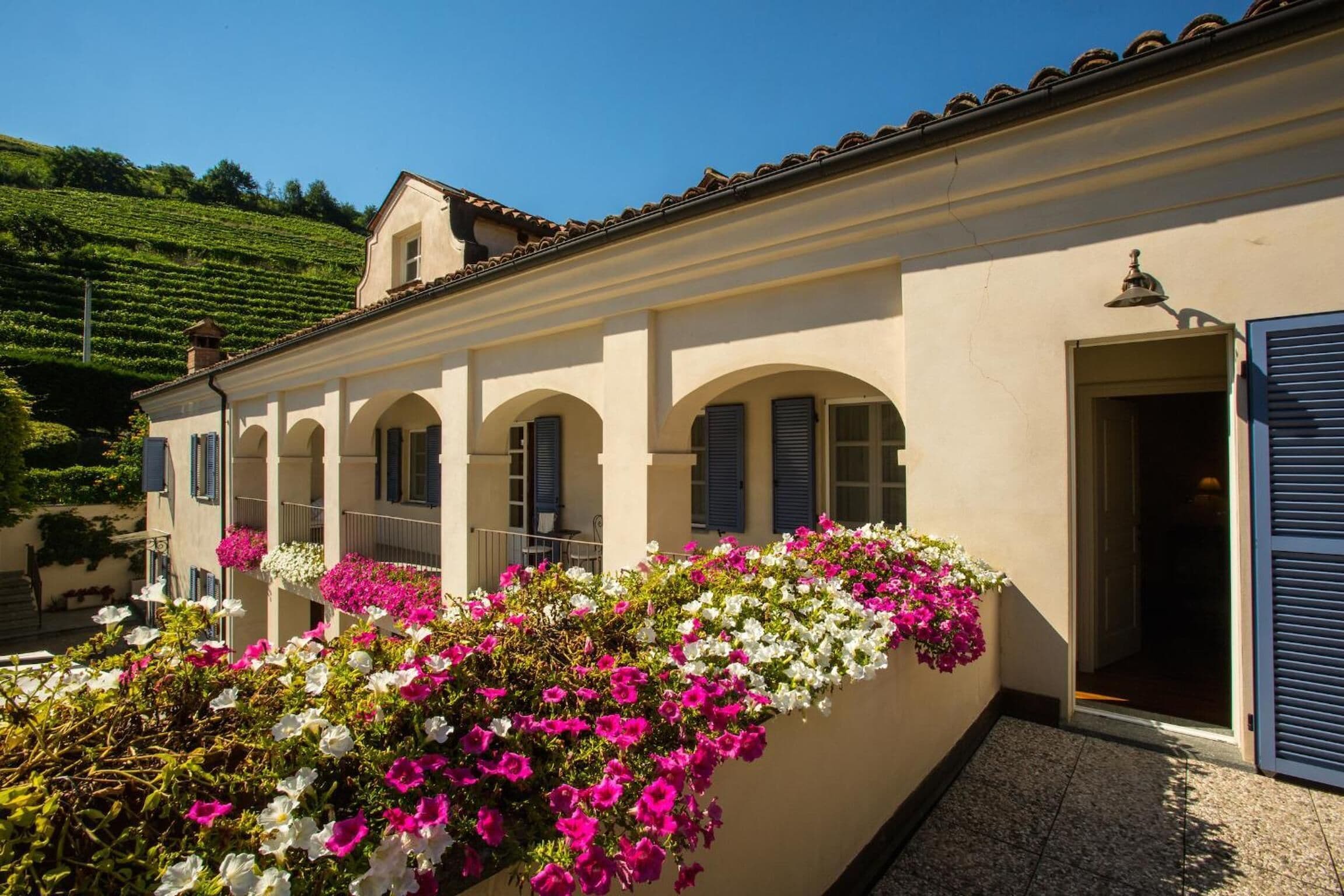 A building with a balcony adorned with colorful flowers, a tiled roof, and a door with a shutter.