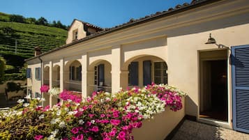 Un edificio con balcón decorado con flores de colores, techo de tejas y puerta con contraventanas.