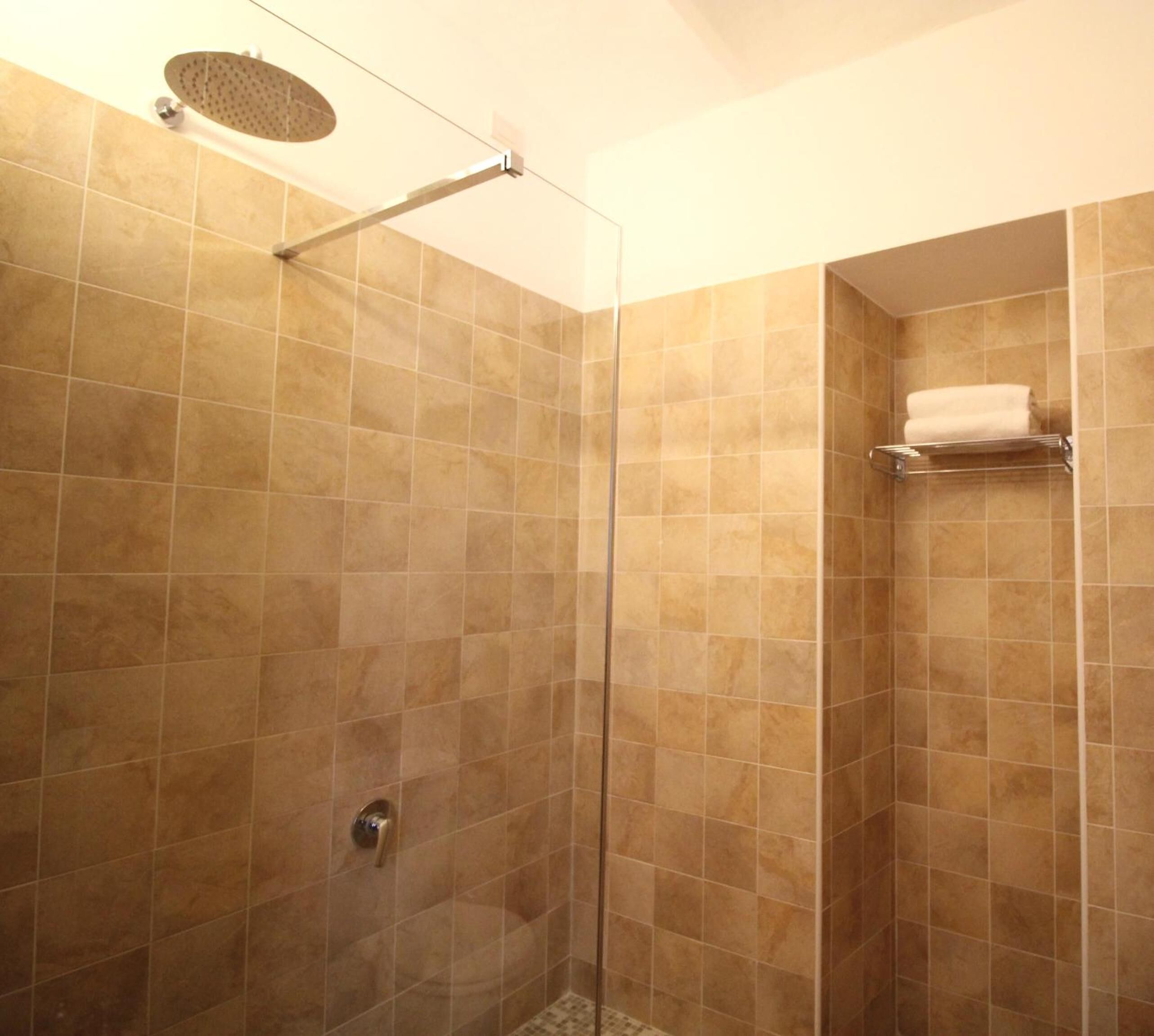 A walk-in shower with beige tiles, a glass door, and a towel rack on the wall.