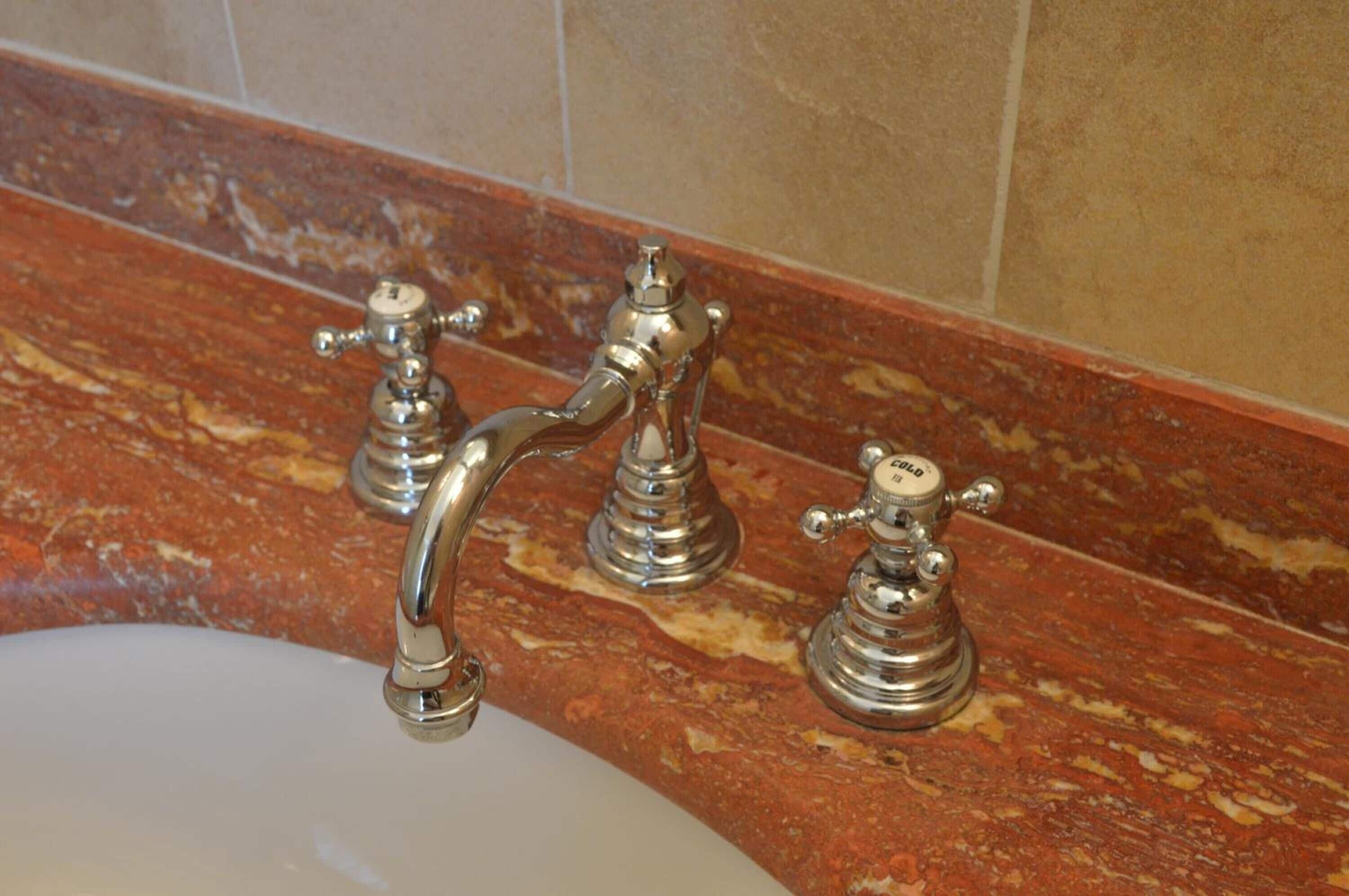 Een badkamer met een marmeren aanrechtblad en drie metalen kraanwerk.