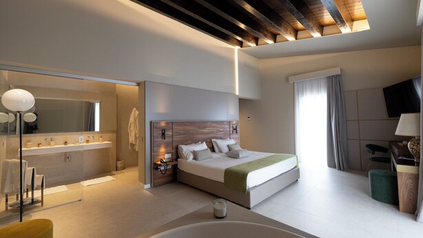 A modern hotel room with a large bed, a separate bathroom, a seating area, and a television.