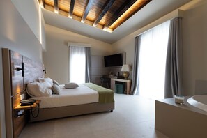 A modern hotel room with a large bed, a desk, a flat-screen TV, a bathroom with a bathtub, and a skylight. - Badiula (Carlentini)