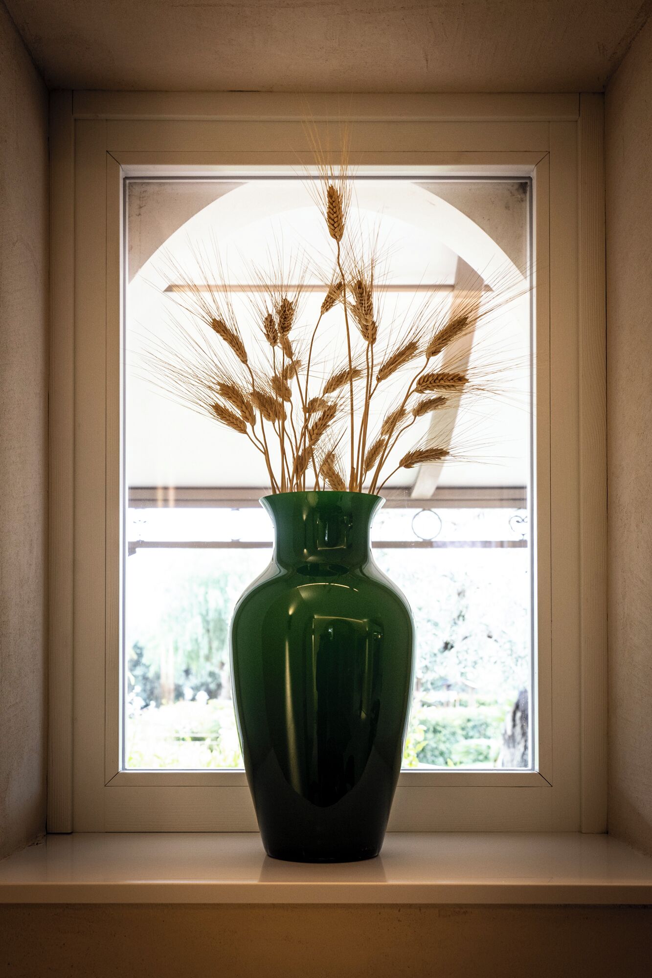 Un vaso verde con spighe di grano su un davanzale.