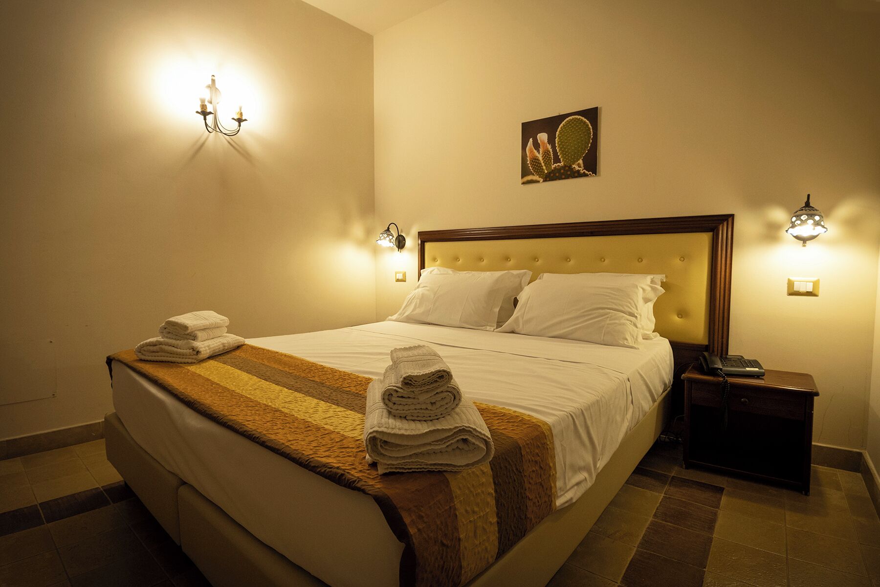 A neatly made bed with towels, a nightstand with a phone, and wall sconces.