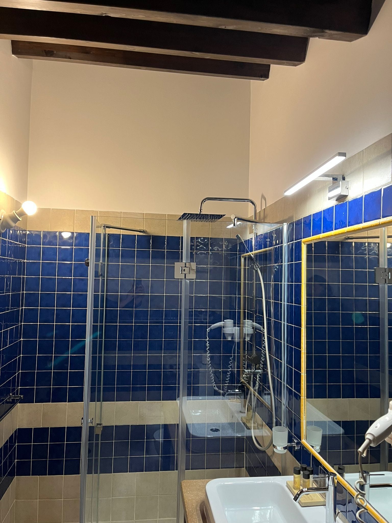 A bathroom with a glass-enclosed shower, a sink with a mirror, and blue-tiled walls.