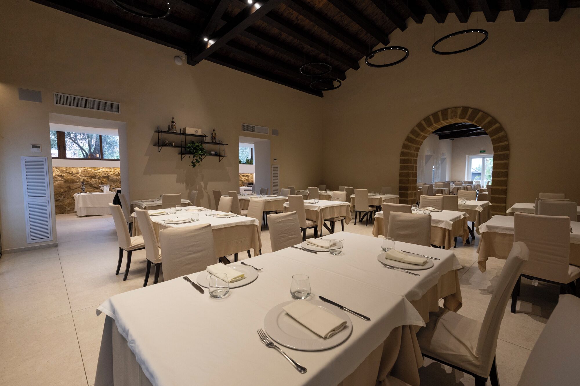A dining area with multiple tables set for guests, featuring a stone wall and arched ceiling.