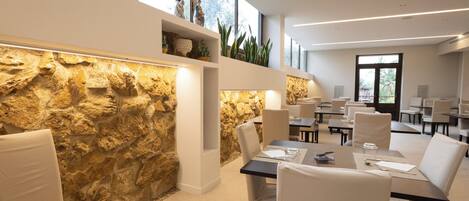 A modern dining area with stone walls, white chairs, and tables.