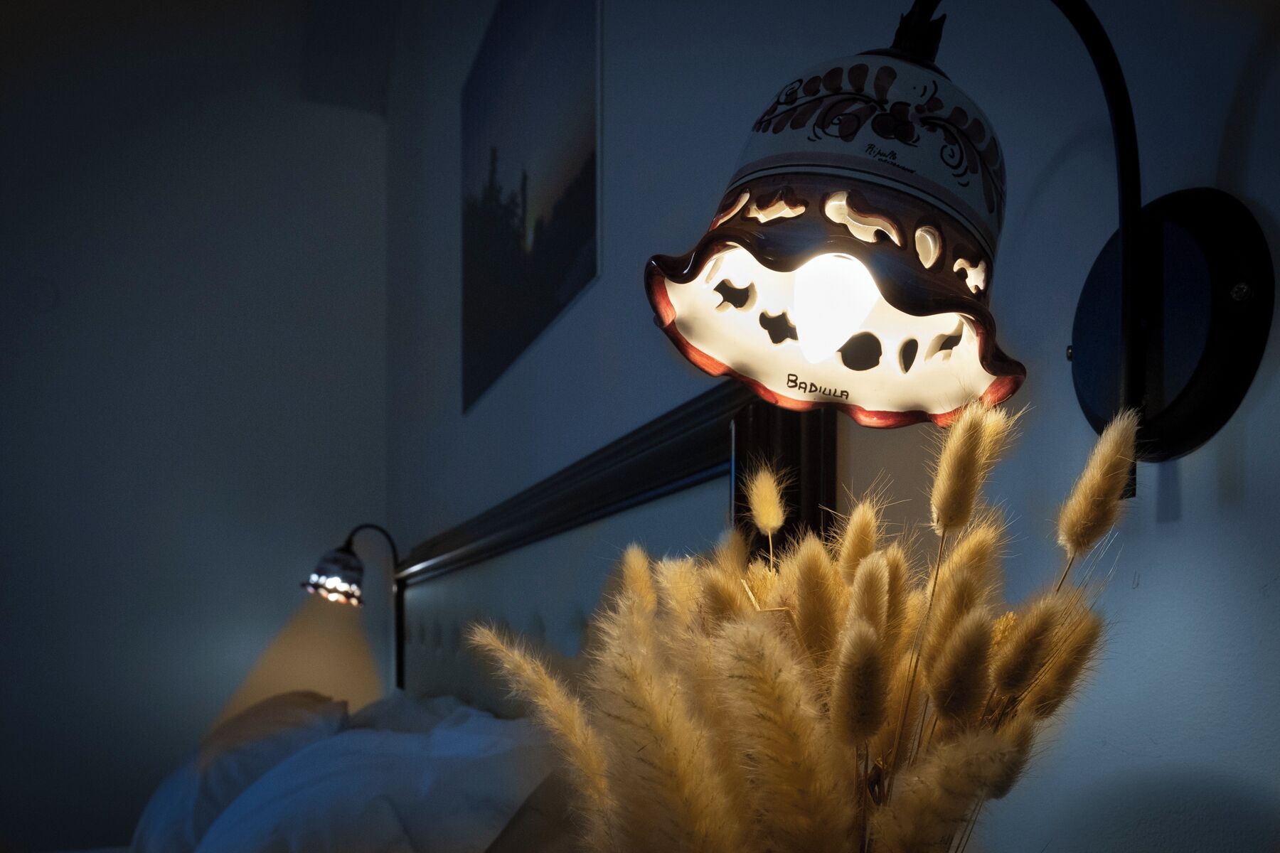 A room with a bed, a wall-mounted lamp, and a decorative wall piece.