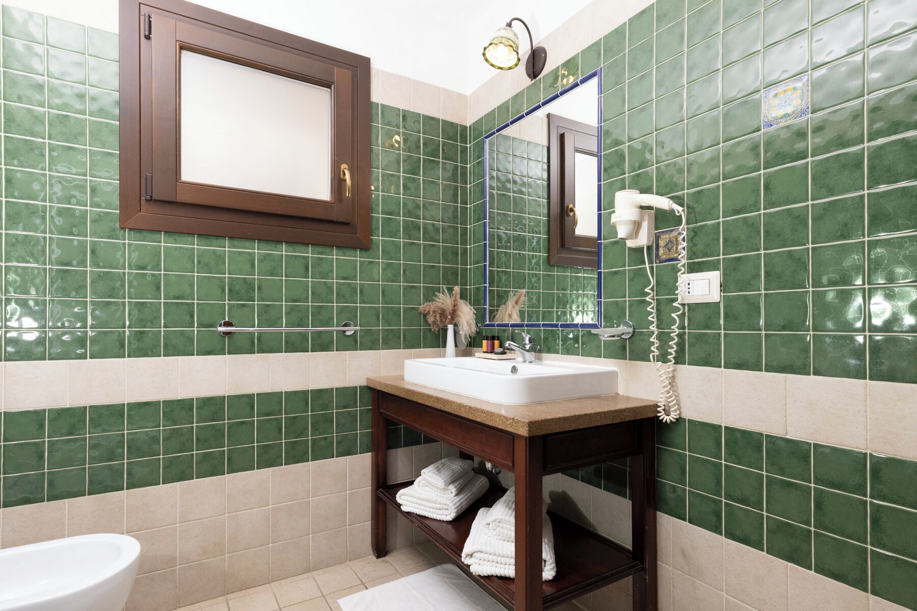 A bathroom with green tiles, a sink, a mirror, a towel rack, and a toilet.