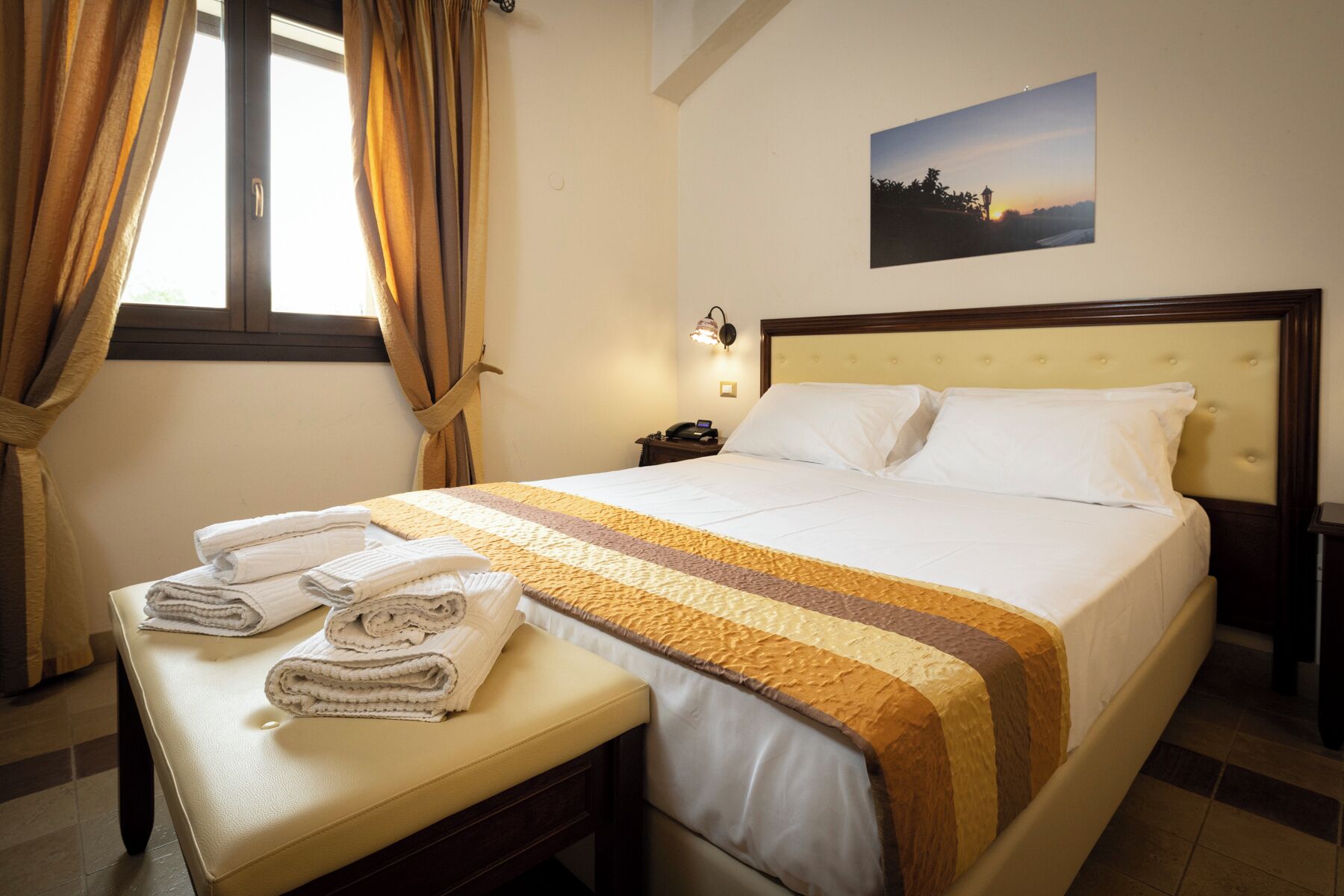 A hotel room with a bed, a bedside table with towels, a nightstand, a lamp, and a picture on the wall.