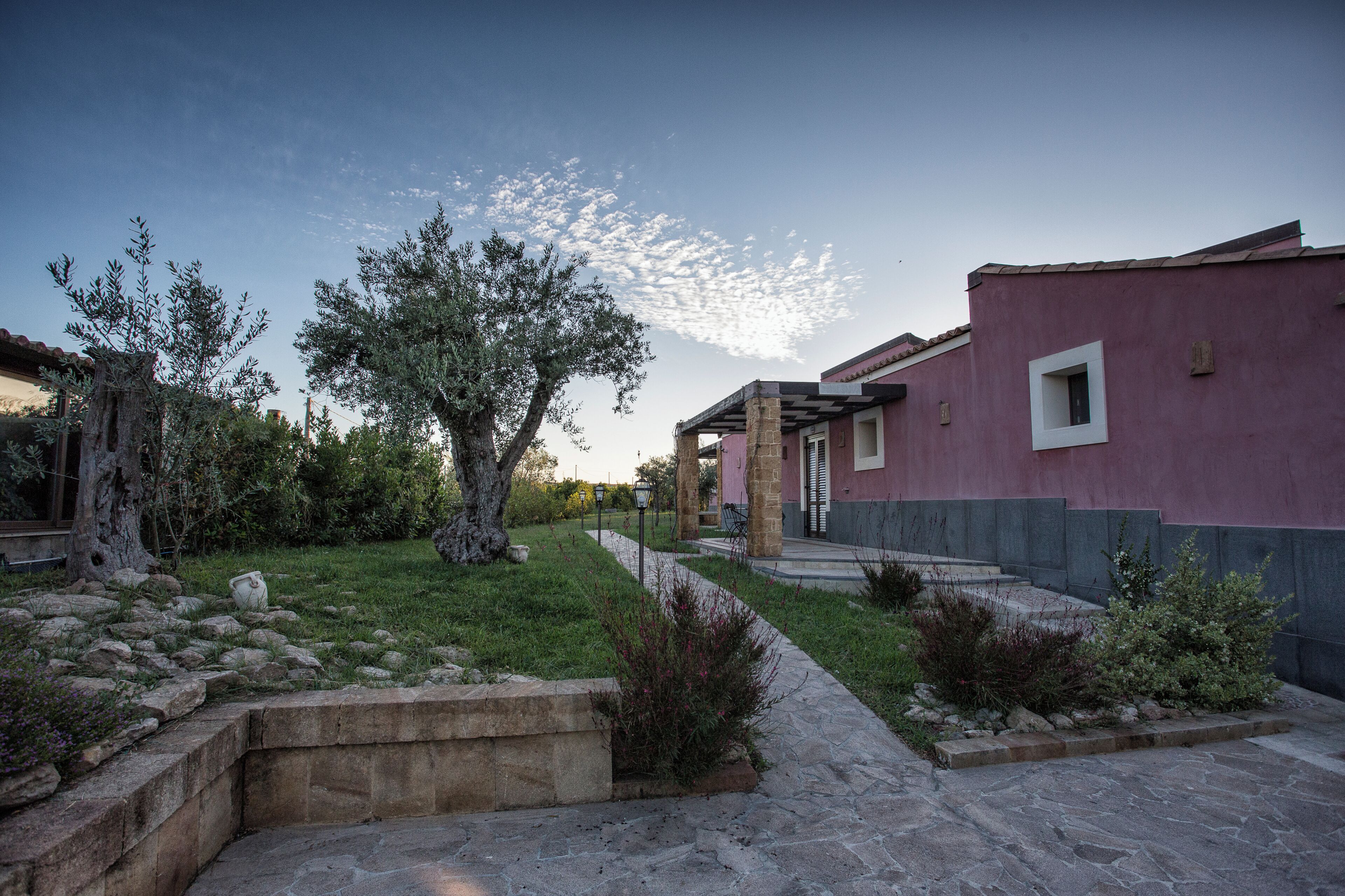 Un cortile con un vialetto in pietra, un albero imponente e un edificio dalla facciata rosa.