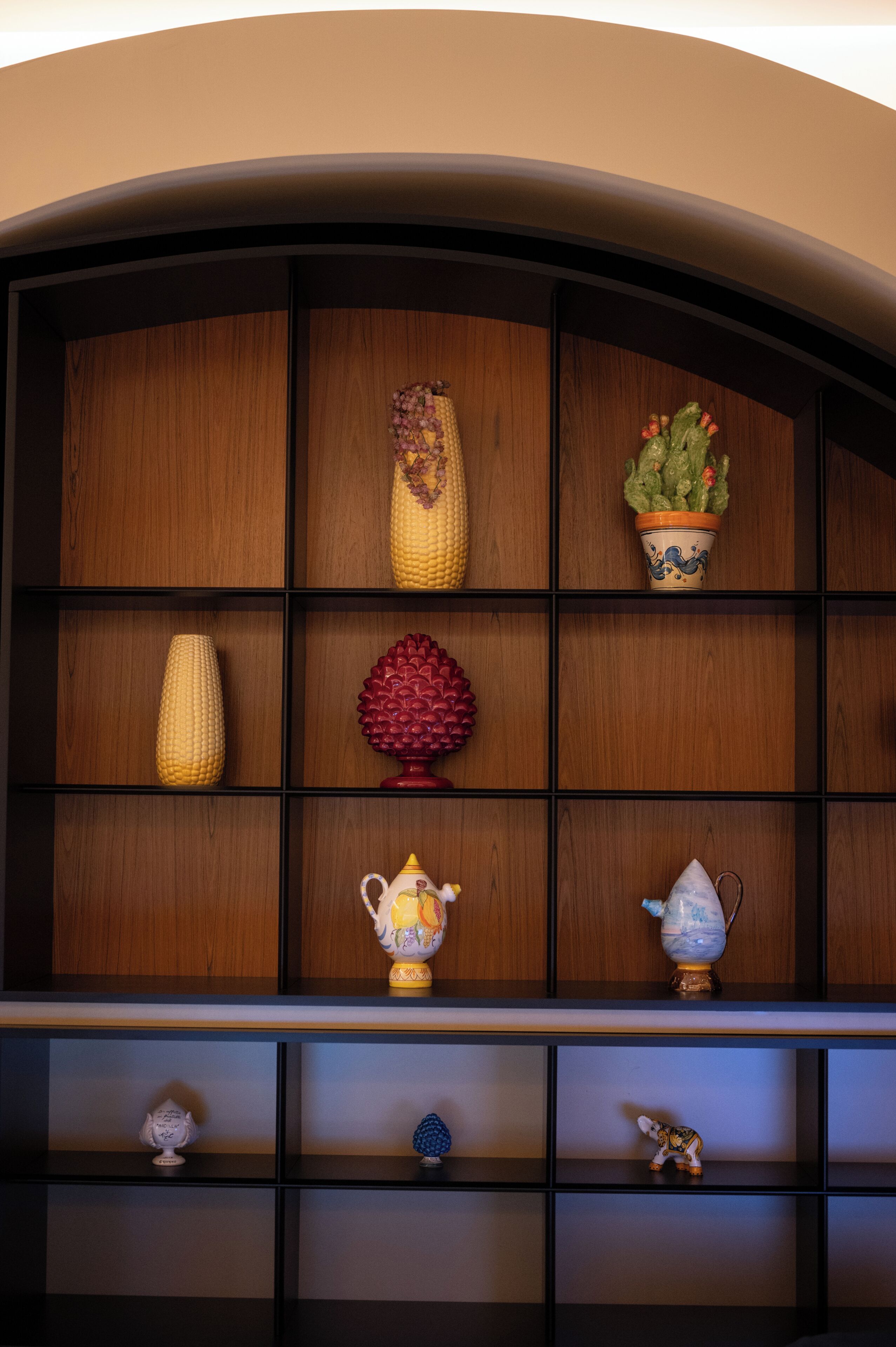 A wooden shelf with decorative items including a corn cob, a red pine cone, and a small figurine.