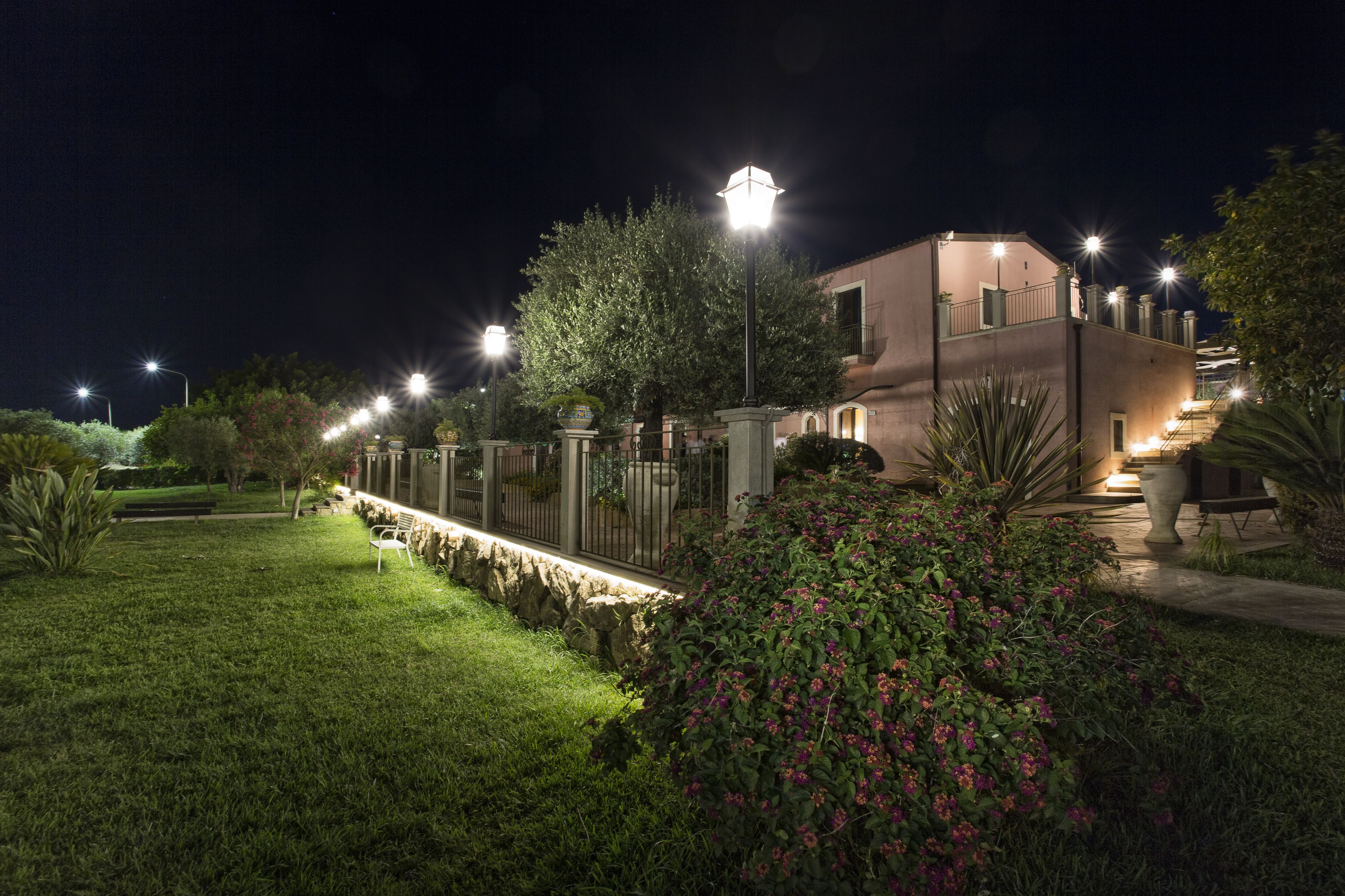 A well-lit residential area with a modern house, a paved pathway, and a neatly trimmed garden.