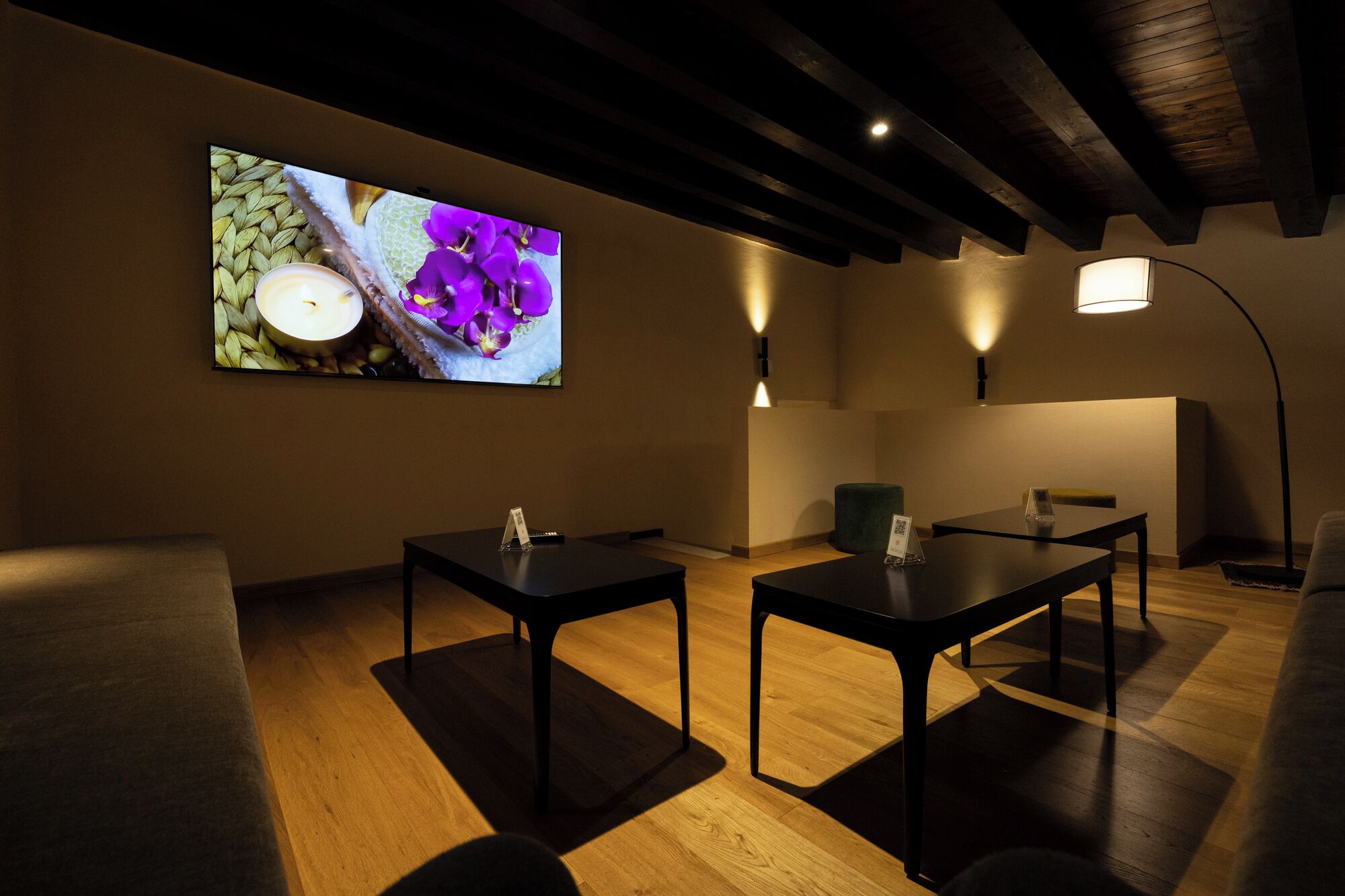 A room with two tables, a sofa, and a wall-mounted TV displaying purple flowers.