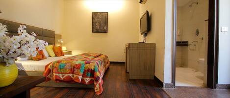 A hotel room with a bed, a wooden nightstand, a TV, a shower area, and a wall-mounted air conditioner.