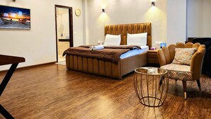 A modern hotel room with a large bed, a small round table, a sofa, and a painting on the wall. - Hotel City Premier (Gurugram)