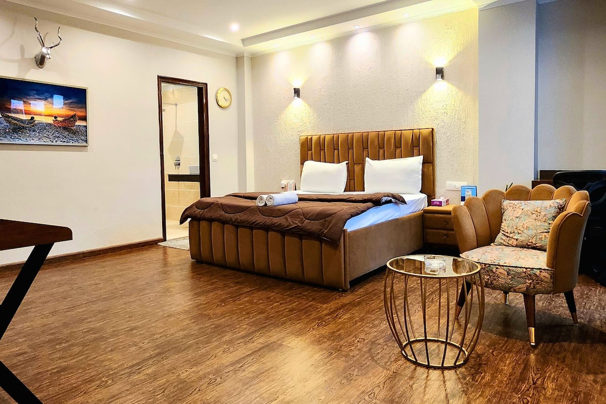 A modern hotel room with a large bed, a small round table, a sofa, and a painting on the wall.