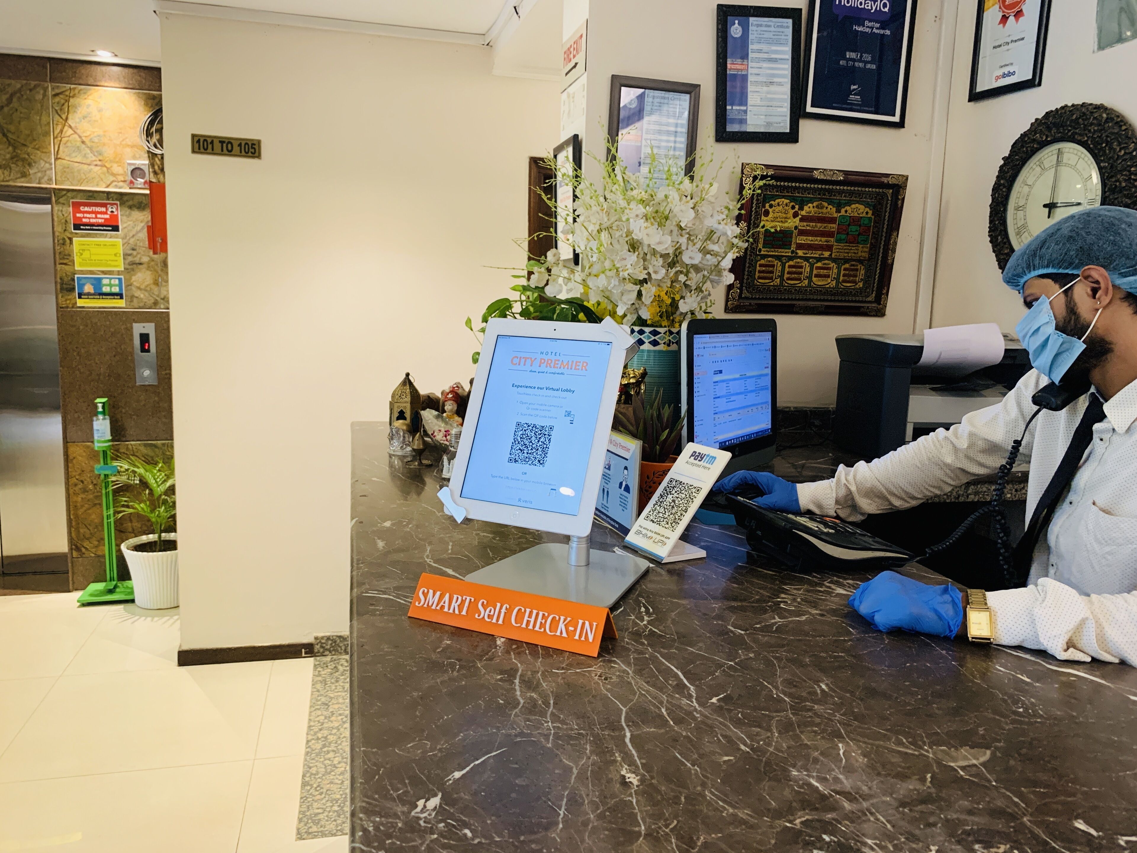 Mostrador de recepción de hotel con una pantalla digital mostrando el mensaje “City Premier”, un letrero que dice “Registro de entrada autónomo inteligente” y un código QR para el pago.
