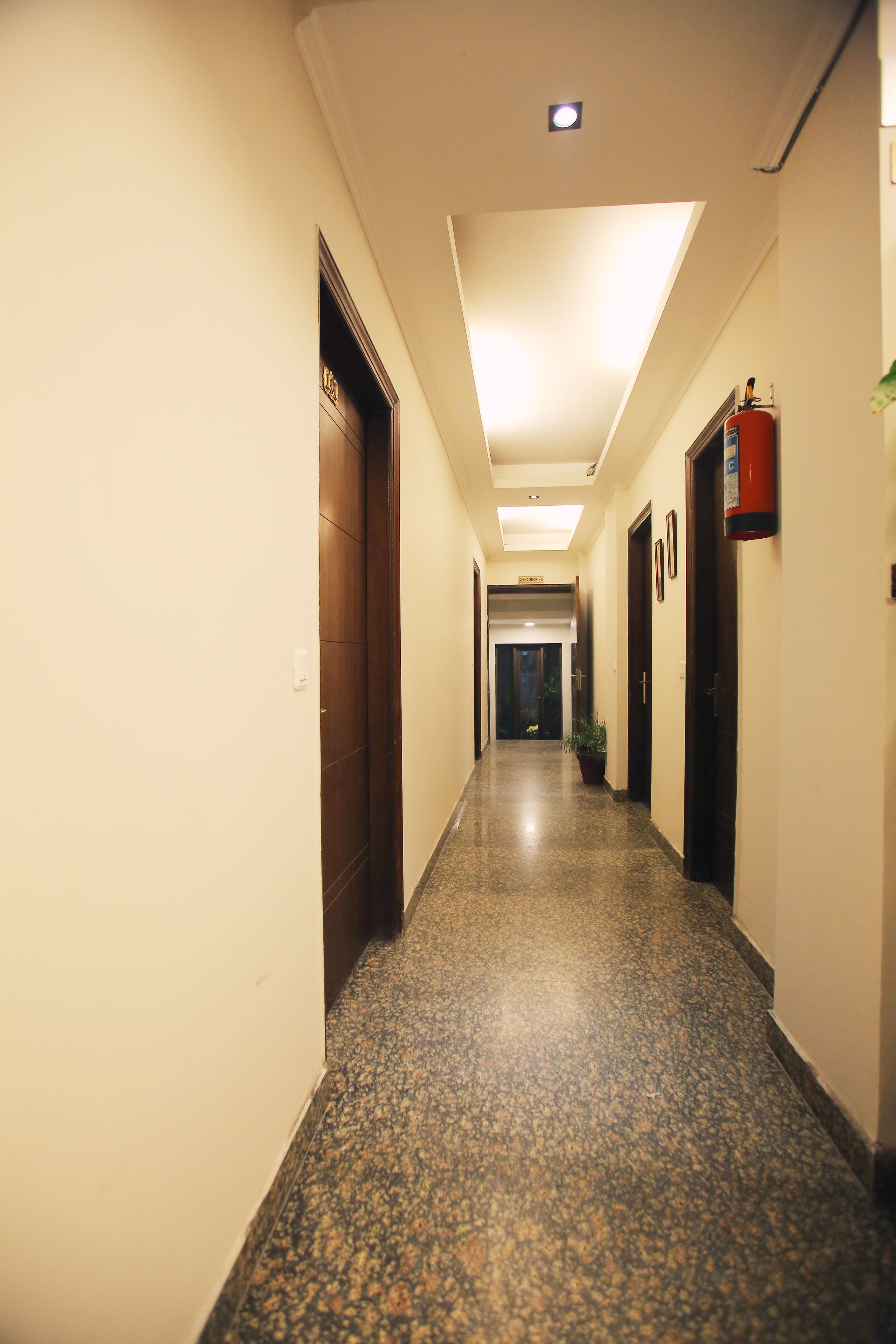 Un pasillo de hotel con piso de mármol, puertas de madera y un extintor en la pared.