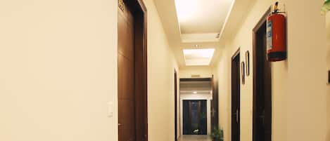 Un pasillo de hotel con piso de mármol, puertas de madera y un extintor en la pared.