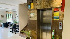 A hotel lobby with a marble wall, an elevator, a reception desk, and a staircase. - Hotel City Premier (Gurugram)