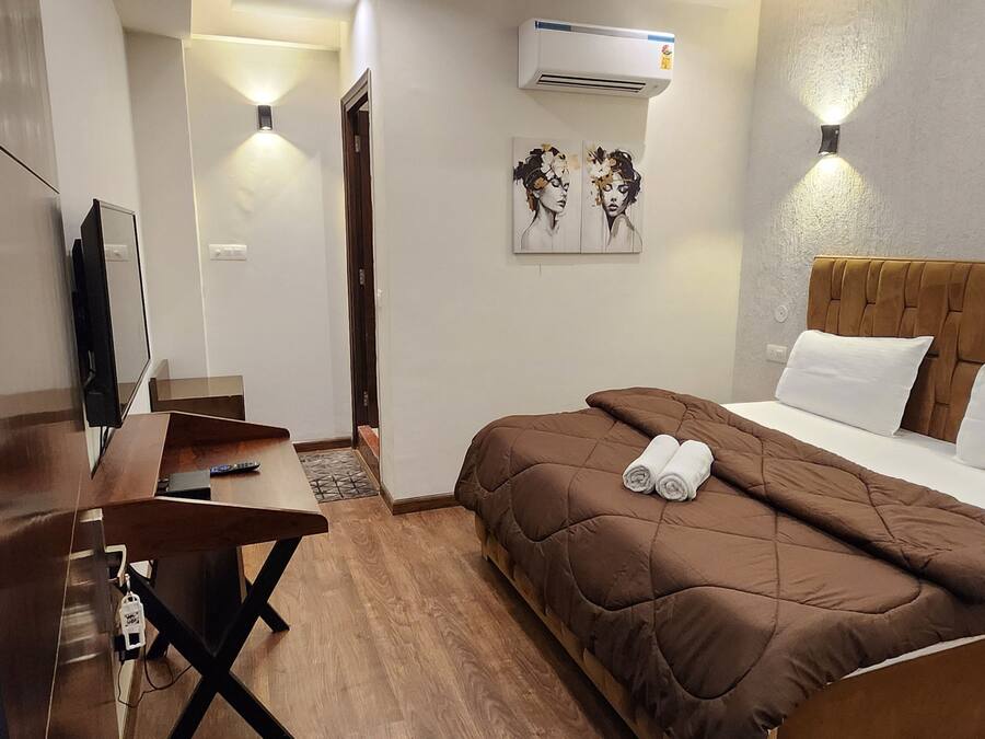 A hotel room with a bed, a desk, a TV, and an air conditioner.