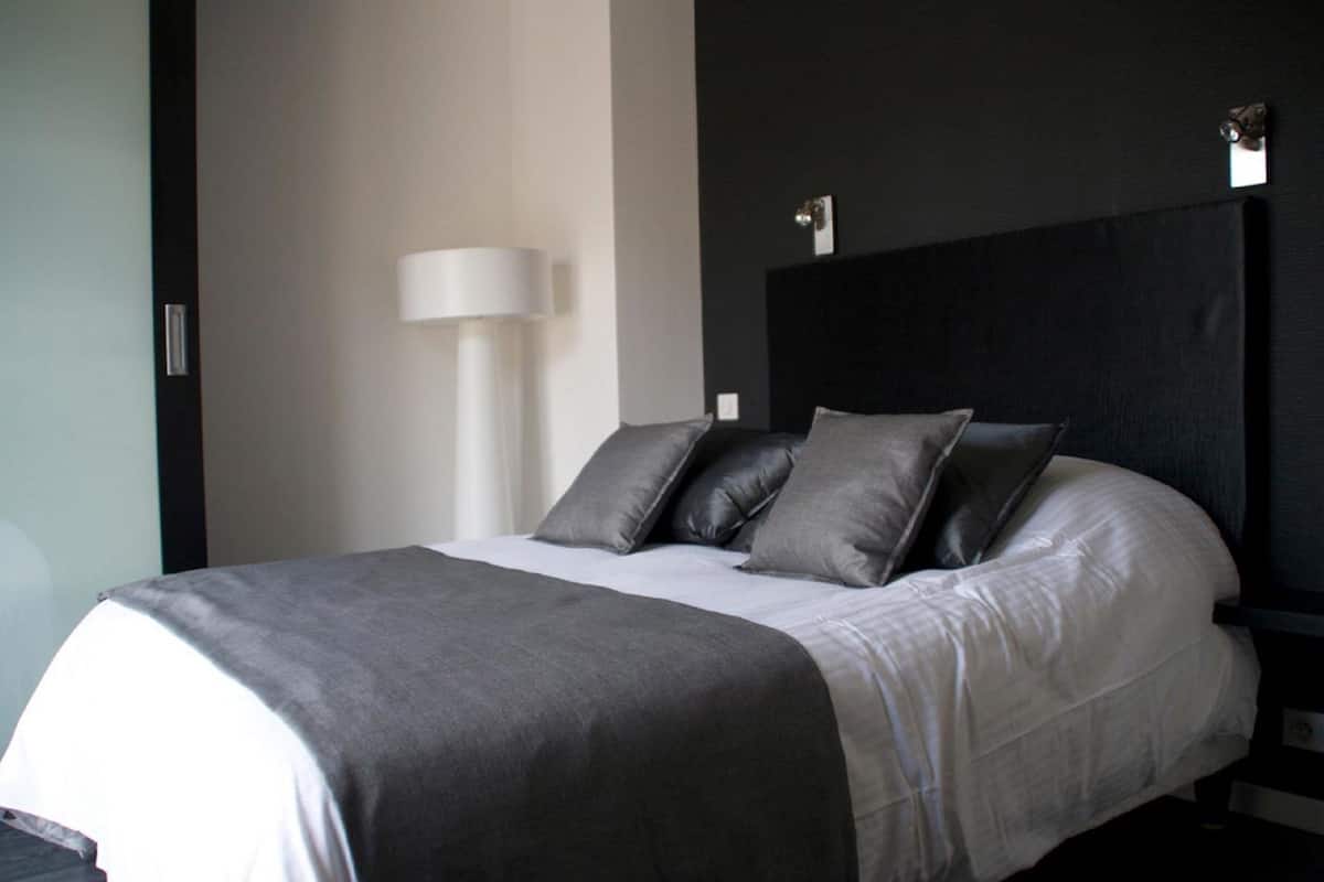Une chambre d’hôtel moderne avec un lit bien fait, une lampe de chevet et une tête de lit sombre.