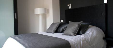 A modern hotel room with a neatly made bed, a bedside lamp, and a dark headboard.
