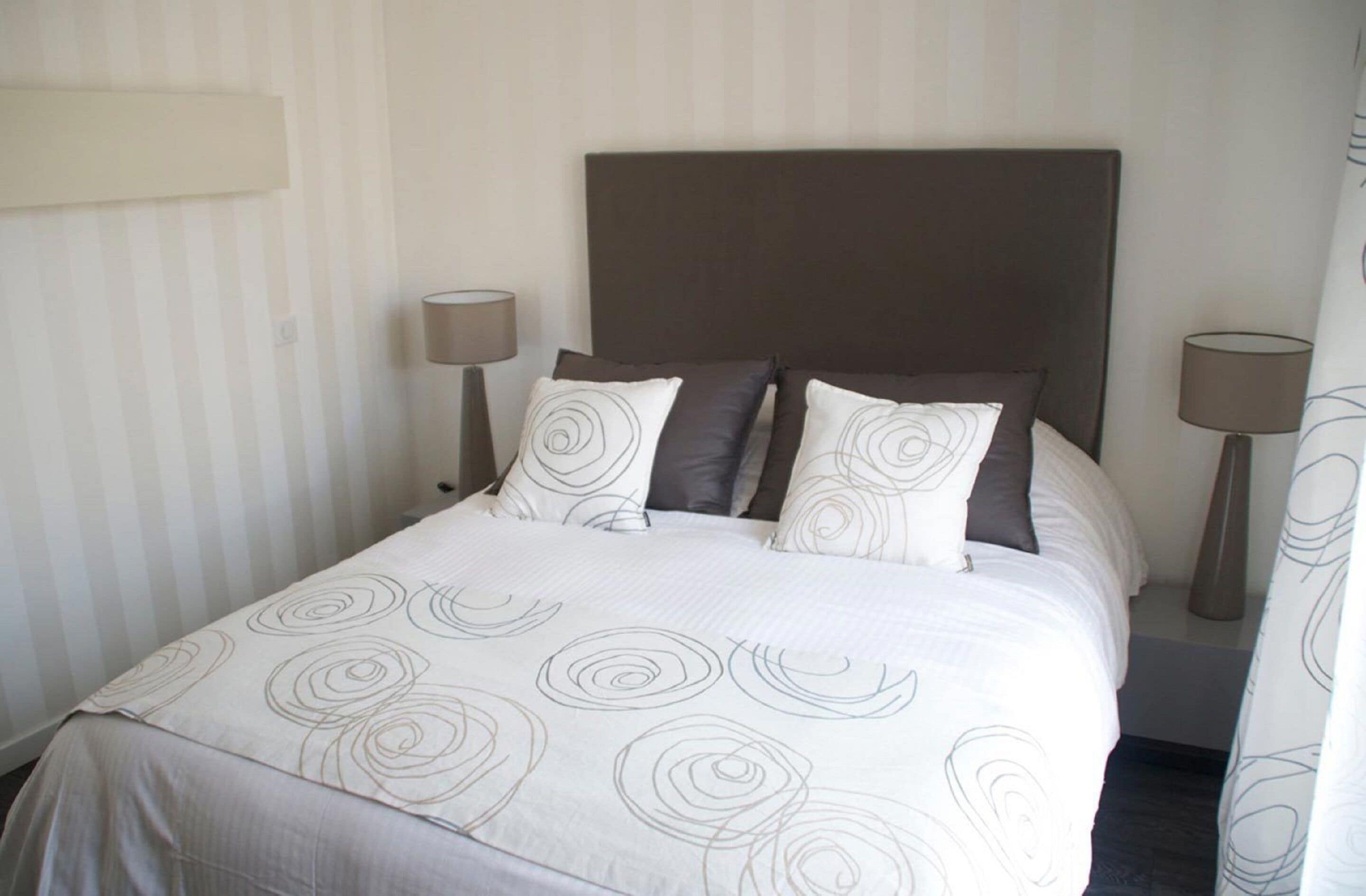 A neatly made bed with a headboard, two bedside lamps, and a striped wall.