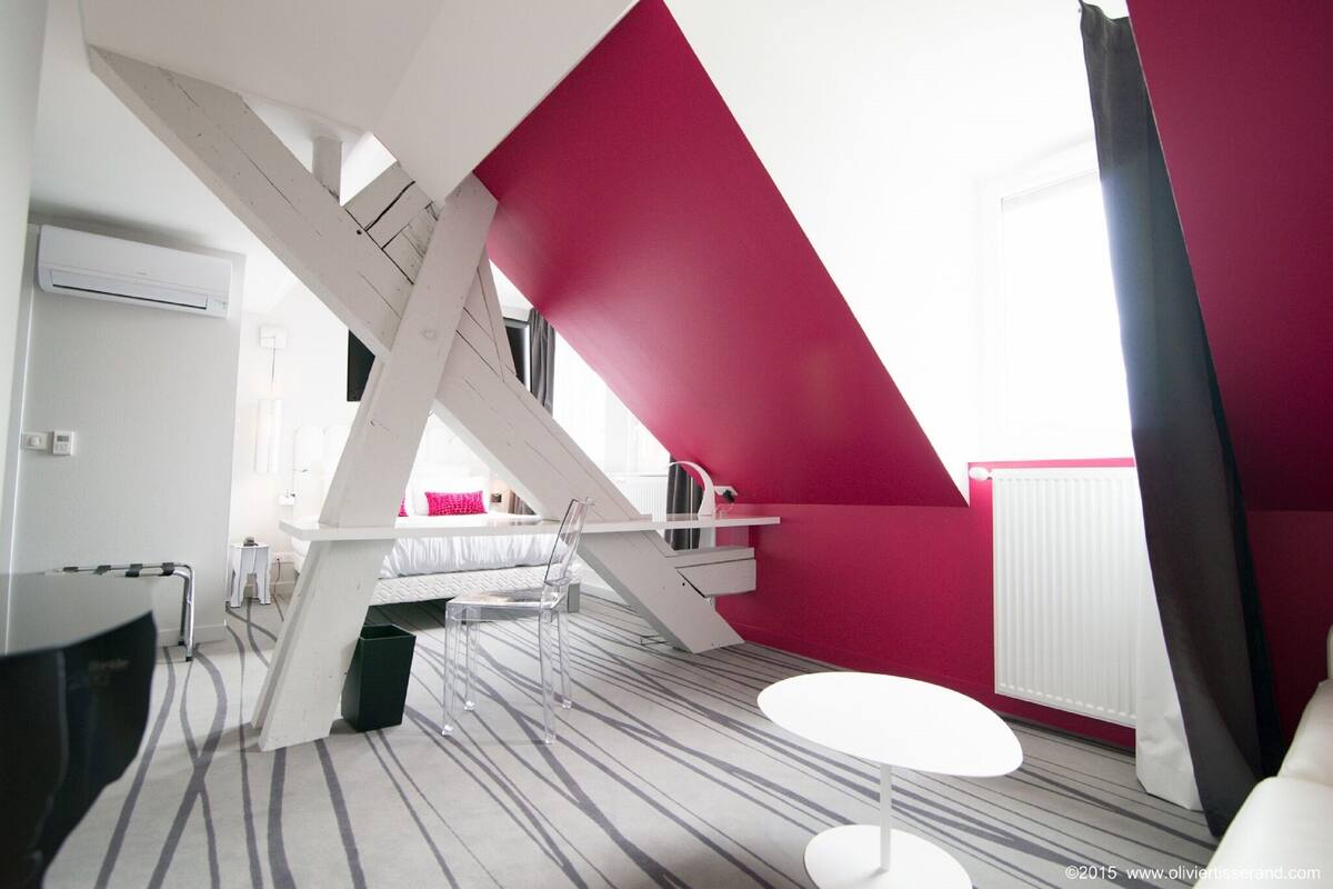 Une chambre d’hôtel moderne dotée d’un plafond à pente au design original, d’un lit, d’un bureau et d’une petite table.
