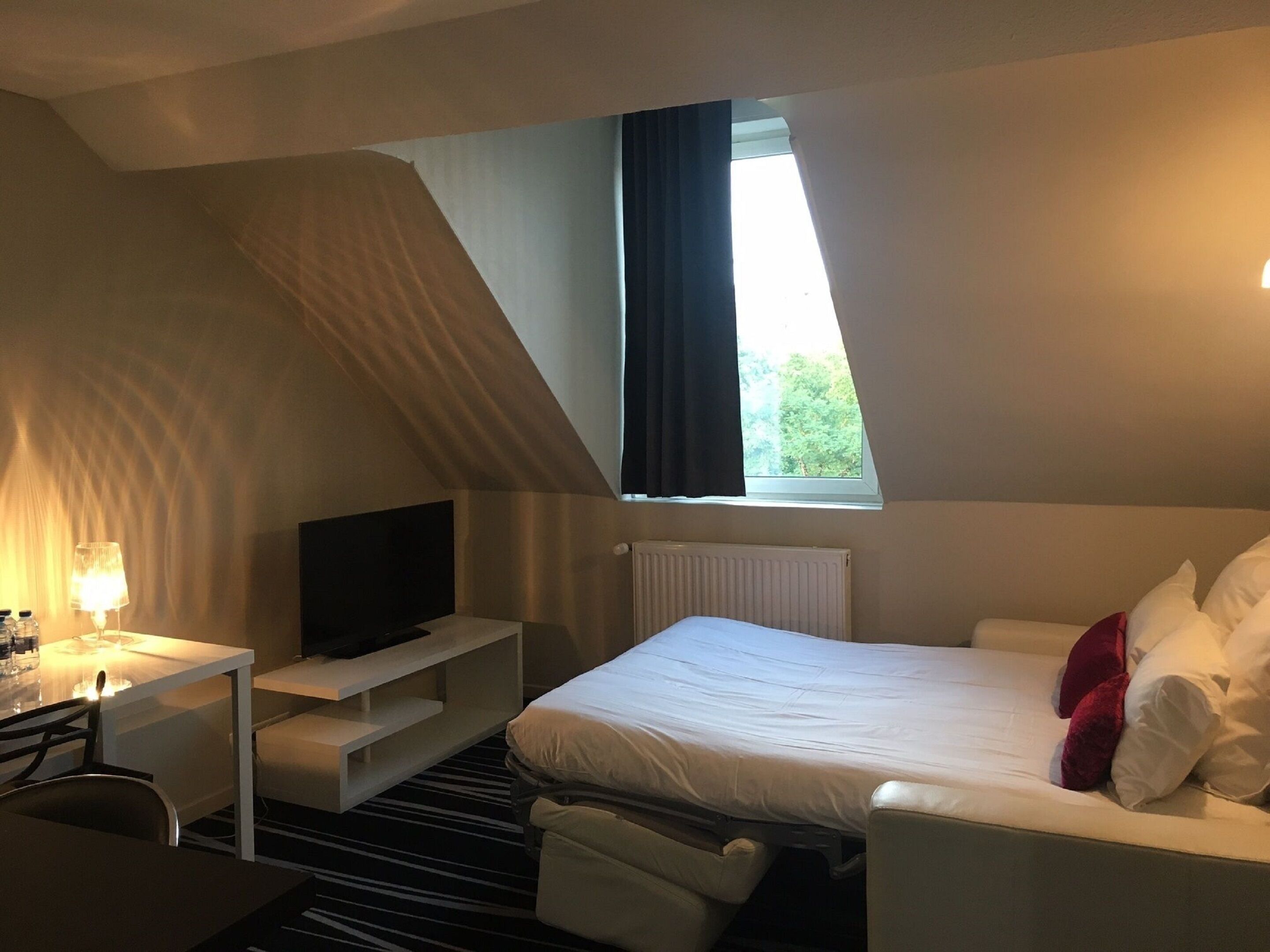 Ein Hotelzimmer mit Bett, Fernseher, Schreibtisch und Fenster mit Blick auf Bäume.
