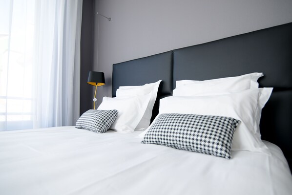 A modern hotel room with a large bed, two pillows, a bedside table, and a lamp.