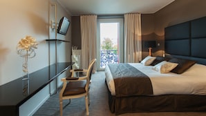 A hotel room with a bed, a desk, a chair, a television, and a view of the outdoors. - Les Capucins (Belfort)