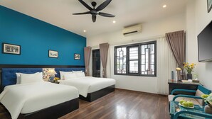 Habitación de hotel con dos camas, un ventilador de techo, un ventanal grande con cortinas, un televisor y una mesita con un florero y manzanas.